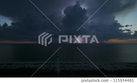White tall lighthouse on sea shore with blinking light at stormy night for commercial vessels navigation. Thunderstorm with lightnings over ocean water posing danger for ships White tall lighthouse on sea shore with blinking light at stormy night for commercial vessels navigation. Thunderstorm with lightnings over ocean water posing danger for ships 115934491