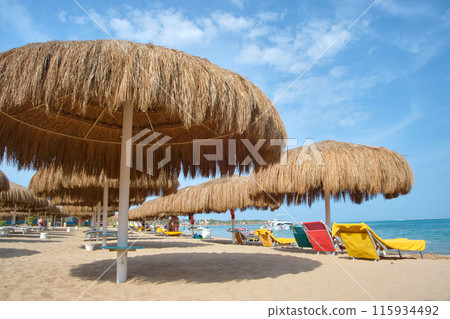 Straw shade umbrella in sea tropical region against blue vibrant sky in summer Straw shade umbrella in sea tropical region against blue vibrant sky in summer 115934492