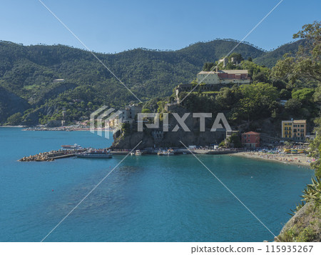 Picturesque view of Monterosso al Mare with beach, colorful houses, train rails, bell tower and Torre Bastioni with green cliffs, clear blue sky and sea. National park Cinque Terre, Liguria, Italy Picturesque view of Monterosso al Mare with beach, colorful houses, train rails, bell tower and Torre Bastioni with green cliffs, clear blue sky and sea. National park Cinque Terre, Liguria, Italy 115935267