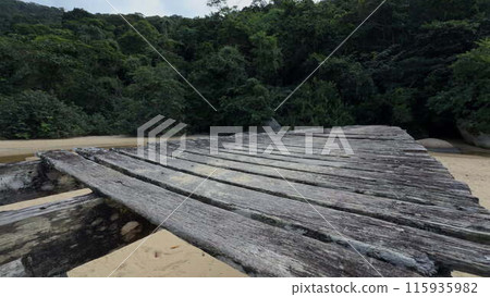 Iconic old wooden bridge over sandy beach in dense green jungle 115935982