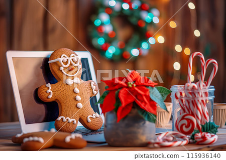 Idea for a Christmas card with a gingerbread man on a laptop, the office is decorated with holly and an Advent wreath, there is a pot of poinsettia flower and candy canes on the table. Idea for a Christmas card with a gingerbread man on a laptop, the office is decorated with holly and an Advent wreath, there is a pot of poinsettia flower and candy canes on the table. 115936140