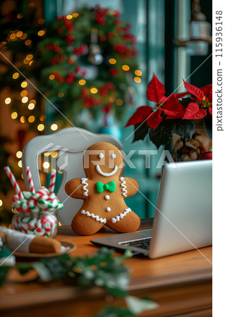 Christmas card with a gingerbread man near the laptop, the office is decorated with a wreath, on the table there is pot with poinsettia flower and a glass of candy canes, a wish for a Merry Christmas 115936148