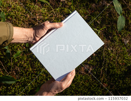 . Hand holding white blank book cover mockup in nature. . Hand holding white blank book cover mockup in nature. 115937032