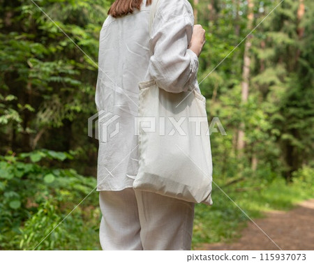 . Tote canvas bag mock up. Woman in linen clothes walking with natural pack, green forest, nature . Tote canvas bag mock up. Woman in linen clothes walking with natural pack, green forest, nature 115937073