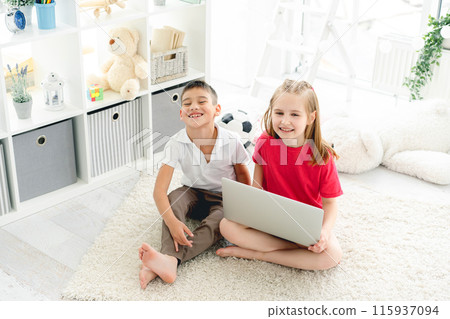 Smiling little friends with laptop on floor in children's room, top view Smiling little friends with laptop on floor in children's room, top view 115937094