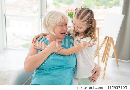 Cute little girl embracing smiling granny in light room Cute little girl embracing smiling granny in light room 115937105