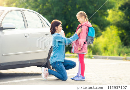 Smiling mother bringing daughter back to school saying goodbye on car parking 115937107