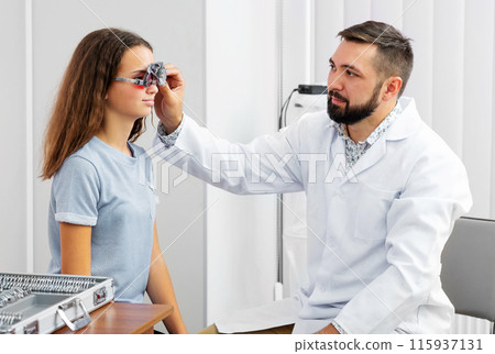 Doctor holding special eye equipment examinating girl's eyes in the ophthalmologic clinic 115937131