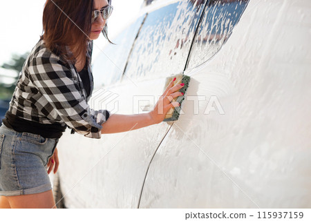 Girl's hand with sponge cleaning car using foam on car wash 115937159