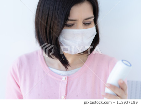 Woman in face mask looking at digital thermometer Woman in face mask looking at digital thermometer 115937189