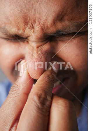 A closeup image showing a man in discomfort, pinching his nose with a pained expression 115937196
