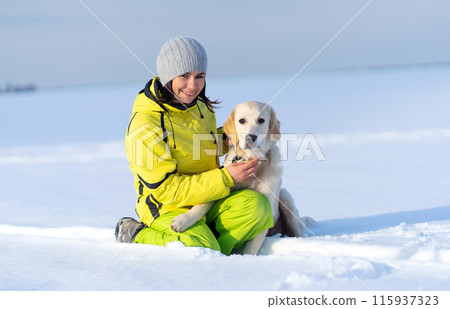 Happy woman caressing cute young retriever dog sitting in snow Happy woman caressing cute young retriever dog sitting in snow 115937323