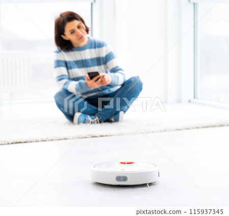 Woman managing automatic vacuum cleaner via smartphone Woman managing automatic vacuum cleaner via smartphone 115937345