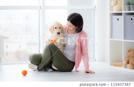 Pretty woman playing with retriever puppy indoors Pretty woman playing with retriever puppy indoors 115937367