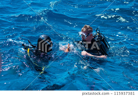 Two professional scuba divers making gestures at sea surface 115937381