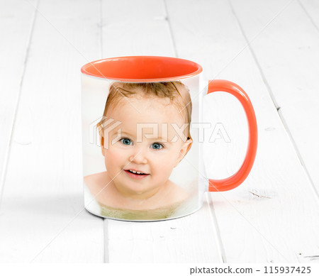 Small orange cup with bright orange handle and a printed face of a baby 115937425