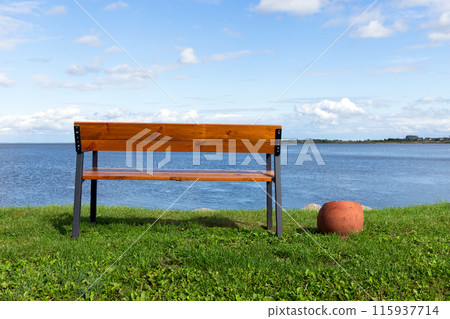 Vacant bench stands on grass at the lake coast Vacant bench stands on grass at the lake coast 115937714