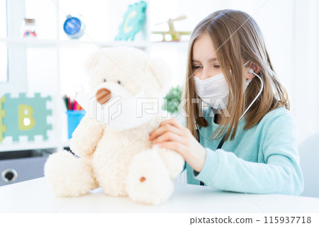 Nice little girl playing in doctor with plush teddy indoors Nice little girl playing in doctor with plush teddy indoors 115937718