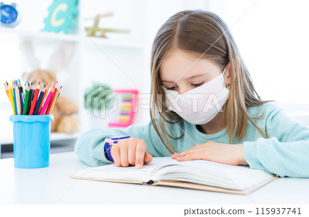 Cute schoolgirl in medical face mask studying at home 115937741