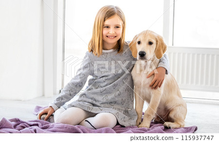 Happy little girl hugging cute dog sitting on floor in light room Happy little girl hugging cute dog sitting on floor in light room 115937747