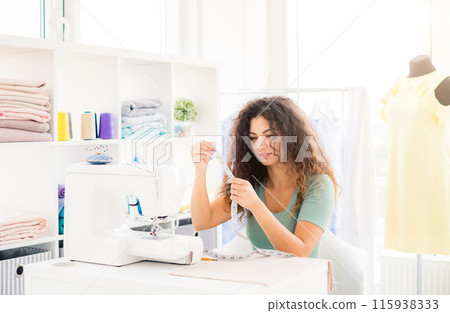 Cute dressmaker holding measuring tape in light workshop Cute dressmaker holding measuring tape in light workshop 115938333