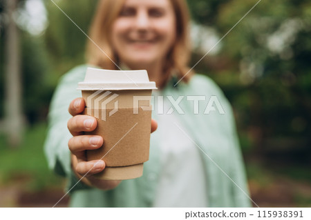 Coffee to go at autumn park. Food, rest, Take away concept. Place logo on mug, mockup. Woman hand holding brown paper cup on park background Coffee to go at autumn park. Food, rest, Take away concept. Place logo on mug, mockup. Woman hand holding brown paper cup on park background 115938391