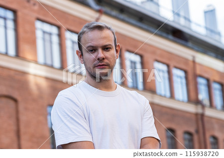 Man with beard and white tshirt stands in front of brick building Man with beard and white tshirt stands in front of brick building 115938720