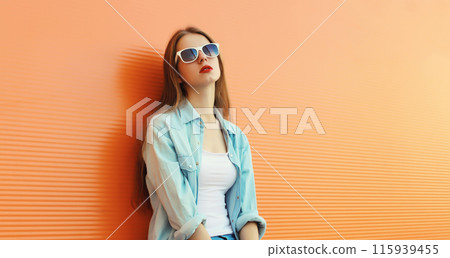 Portrait of modern stylish young woman in white glasses, casual clothing posing on orange background Portrait of modern stylish young woman in white glasses, casual clothing posing on orange background 115939455