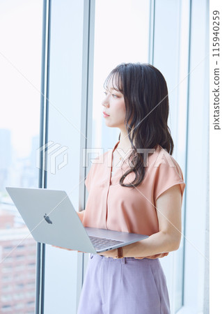 Woman looking at a computer by the window in an office 115940259