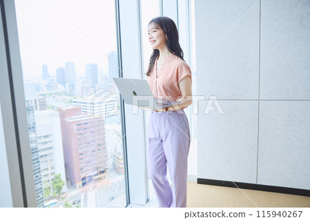 Woman looking at a computer by the window in an office 115940267