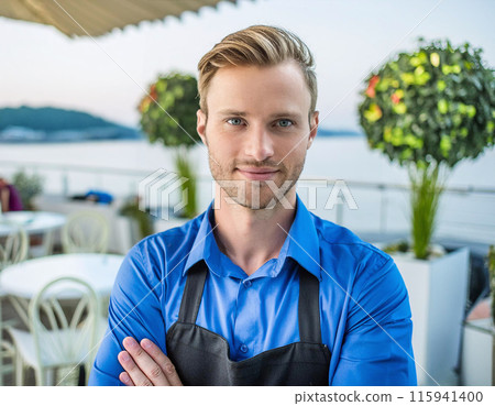 Confident Young Waiter in Blue Shirt at Outdoor Restaurant with Scenic View 115941400