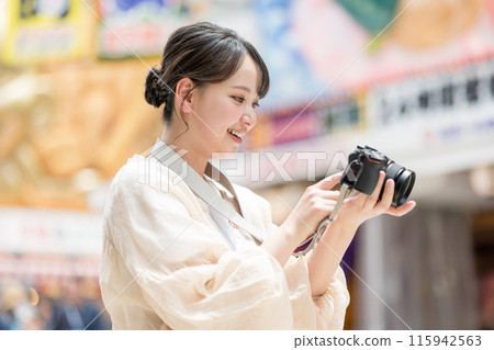A girl with a camera taking pictures with her hobby single-lens reflex camera while sightseeing in the downtown area of the city | Photographer image 115942563