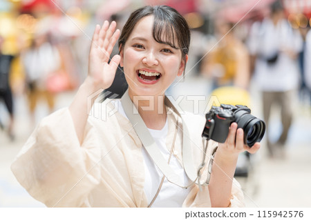 A camera girl taking pictures with her hobby single-lens reflex camera while sightseeing in the downtown area of the city | Meeting image | Photographer image 115942576