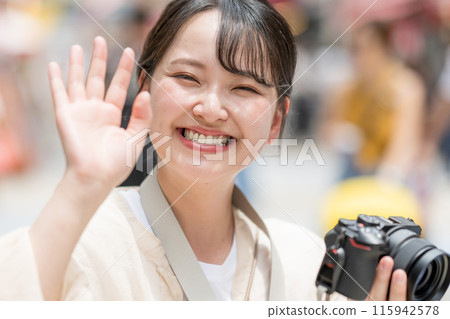 A camera girl taking pictures with her hobby single-lens reflex camera while sightseeing in the downtown area of the city | Meeting image | Photographer image 115942578