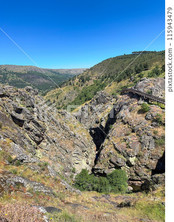 A serene valley with a wooden path, embraced by rocky cliffs A serene valley with a wooden path, embraced by rocky cliffs 115943479