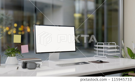 A modern office features a computer with a white-screen mockup and office supplies on a white desk. A modern office features a computer with a white-screen mockup and office supplies on a white desk. 115945733