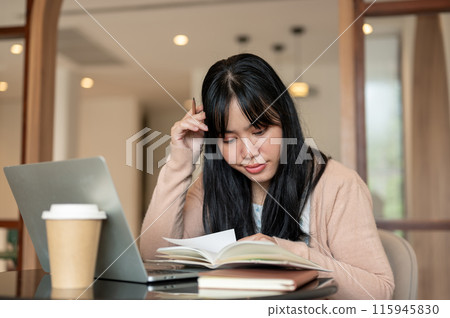 A thoughtful Asian female college student is focusing on working on her project, reading a book. 115945830