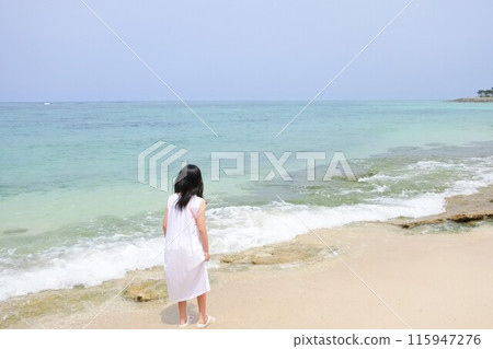 A girl wearing a dress standing on the beach 115947276