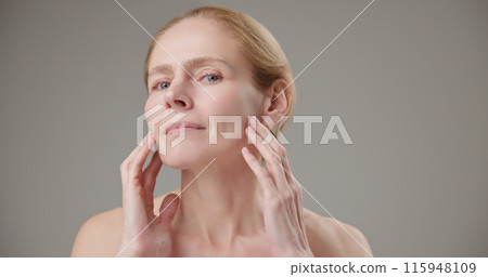 Anti age, Beauty, health and dry skin care concept - beautiful middle-aged mature Caucasian woman in her 50s touching her face skin and looking at the camera with a slight smile Anti age, Beauty, health and dry skin care concept - beautiful middle-aged mature Caucasian woman in her 50s touching her face skin and looking at the camera with a slight smile 115948109