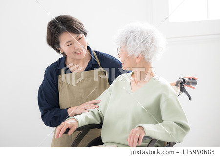 A senior in a wheelchair and a woman who cares for him. A mother and daughter looking at each other at home 115950683