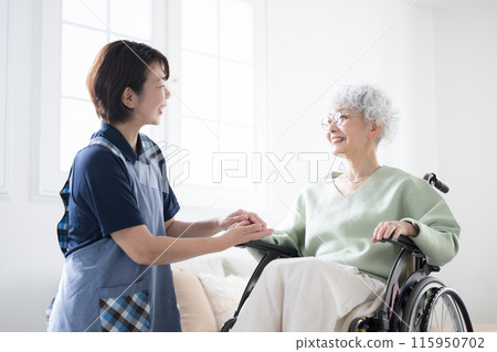 A caregiver holds the hand of a senior woman in a wheelchair as they look at each other A caregiver holds the hand of a senior woman in a wheelchair as they look at each other 115950702