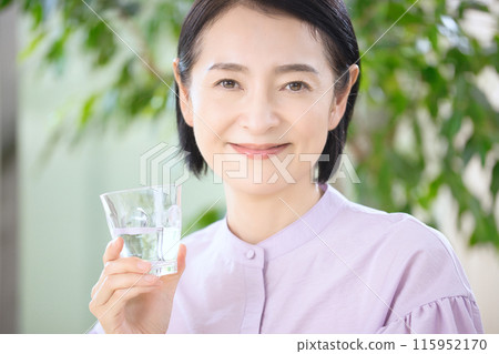 Smiling middle-aged woman drinking water in the living room 115952170