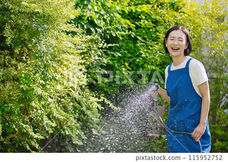 A smiling middle-aged woman watering the greenery in her garden A smiling middle-aged woman watering the greenery in her garden 115952752