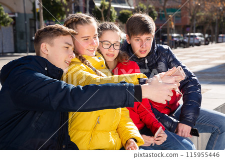 Four young happy teenagers taking self picture using mobile phone outdoors Four young happy teenagers taking self picture using mobile phone outdoors 115955446