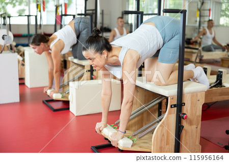 Young girl doing exercises standing on knees on combo chair Young girl doing exercises standing on knees on combo chair 115956164