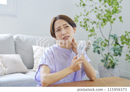 A woman using a portable fan in a humid living room 115956373