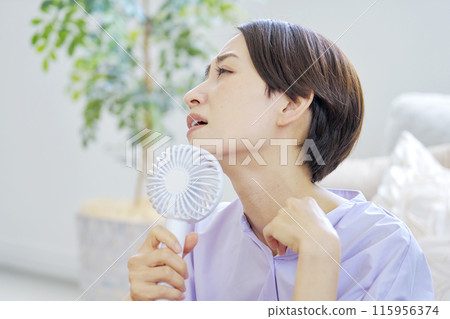 一位女士在潮濕的客廳使用便攜式風扇 115956374