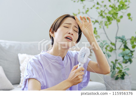一位女士在潮濕的客廳使用便攜式風扇 115956376