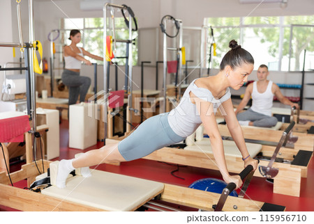 Young girl doing full body exercises lying on reformer device 115956710
