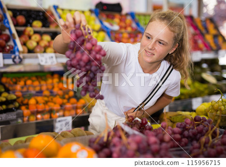 Portrait of a fifteen-year-old girl chooses grapes, holding bunches 115956715